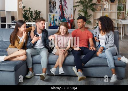 Passer un bon moment ensemble. Groupe de jeunes gens multiculturels heureux dans l'ambiance décontractée se moque en s'asseyant ensemble sur le canapé à la maison. Ils Banque D'Images