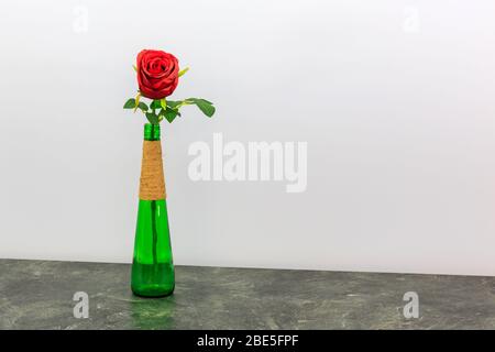 Une rose rouge dans une grande bouteille verte avec fond bleu clair Banque D'Images