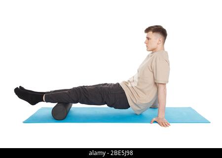 Beau homme montre des exercices à l'aide d'un rouleau en mousse pour un massage de libération myofasciale des points de déclenchement. Massage du muscle de la tibia. Isolé sur blanc. Banque D'Images