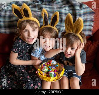 Emily (à gauche),9, Daisy (au centre),7, et Benjamin,3, après une chasse aux œufs le dimanche de Pâques, confinée à leur maison à Bromley, au sud de Londres, alors que le Royaume-Uni continue de se maintenir en position pour aider à freiner la propagation du coronavirus. Banque D'Images