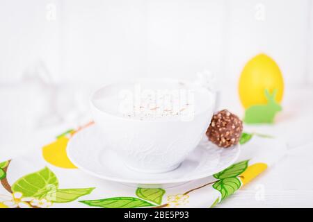 Tasse de café cappuccino en porcelaine blanche avec cannelle, bonbons au chocolat et décorations de Pâques. Couleurs de printemps Banque D'Images