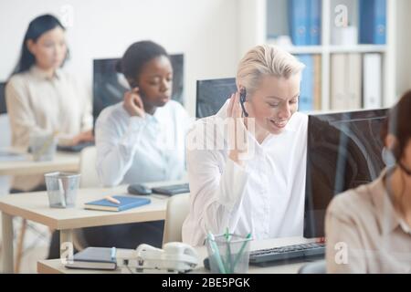 Portrait des opérateurs de hotline femmes assis en ligne sur les bureaux , se concentrer sur le sourire jeune femme parler au client via casque, espace de copie Banque D'Images