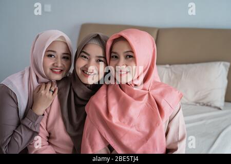 souriant trois femmes de hijab assis sur le lit dans la chambre quand on regarde l'appareil photo Banque D'Images