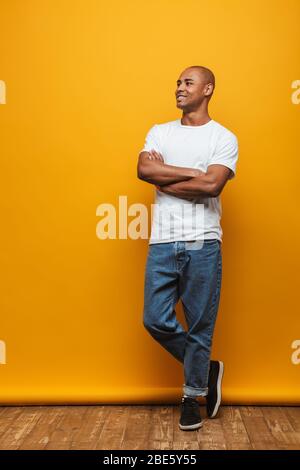 Portrait complet d'un jeune homme décontracté et heureux et heureux, debout sur fond jaune, bras repliés Banque D'Images