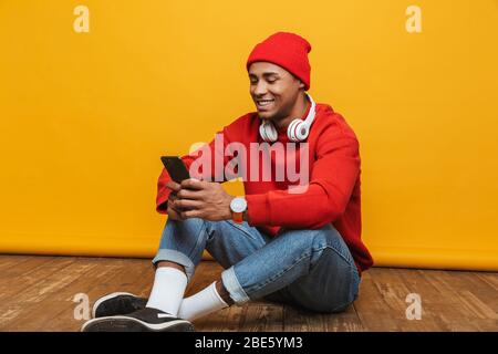 Portrait d'un jeune homme africain agréable et décontracté assis sur un étage sur fond jaune Banque D'Images