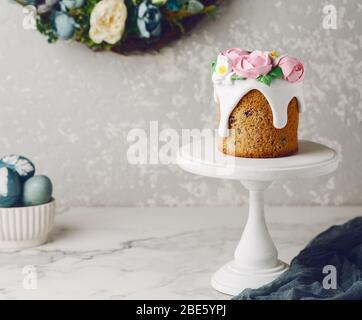 Gâteau de Pâques sur un stand blanc avec roses roses crémeuses roses. Table en marbre avec œufs peints en bleu. Couronne fleurie sur le mur. Vacances Banque D'Images