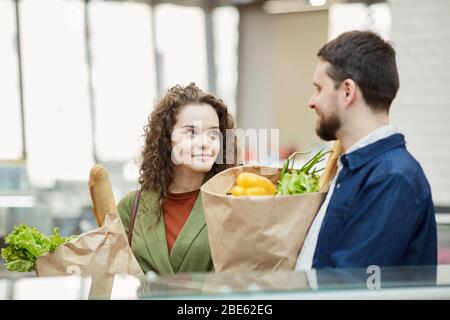 Taille en haut portrait de couple adulte moderne tenant des sacs en papier avec des articles d'épicerie tout en profitant des magasins dans un supermarché, espace de copie Banque D'Images