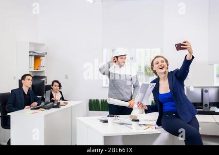 Les employés qui s'amusent au bureau, se posent et prennent des selfies avec un smartphone. Banque D'Images