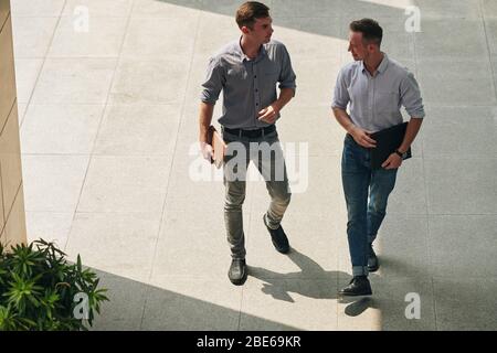De sérieux beaux jeunes hommes d'affaires marchant à la construction de bureaux et discutant de projet Banque D'Images