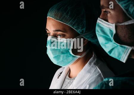 Près de deux médecins de sexe féminin et masculin travaillant avec un masque chirurgical médical, une casquette médicale et des vêtements de protection contre les virus sur fond noir avec co Banque D'Images