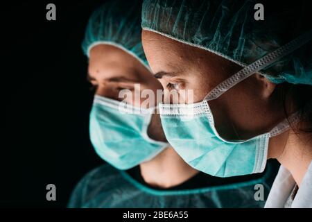 Près de deux médecins de sexe féminin et masculin travaillant avec un masque chirurgical médical, une casquette médicale et des vêtements de protection contre les virus sur fond noir avec co Banque D'Images