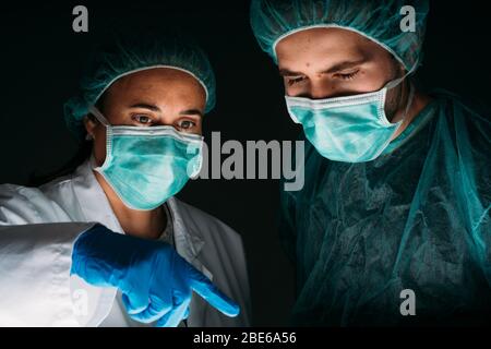 Portrait de gros plan de deux médecins femmes et hommes travaillant avec un masque chirurgical médical, une casquette médicale et des vêtements de protection contre les virus sur le dos noir Banque D'Images