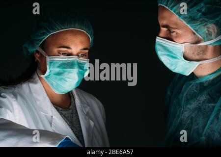 Portrait de gros plan de deux médecins femmes et hommes travaillant avec un masque chirurgical médical, une casquette médicale et des vêtements de protection contre les virus sur le dos noir Banque D'Images