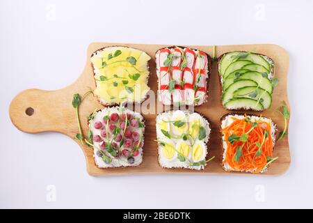 Six sandwichs sur pain grillé avec carottes fraîches, concombres, ananas, cassis rouge, bâtonnets de crabe et œufs de caille avec microgreens de pois sur planche en bois Banque D'Images