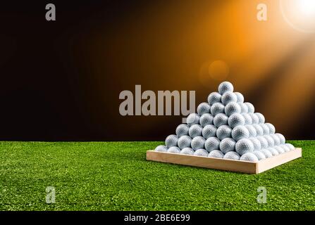 Pyramide de balles de golf dans un terrain de conduite avec lumière orange brillant, image horizontale Banque D'Images