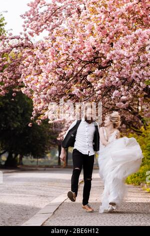 des jeunes mariés joyeux qui naissent dans la ville sont heureux parmi les arbres fleuris. Les jeunes mariés ont du plaisir à passer leur temps dans une belle ville. Mariage en spr Banque D'Images