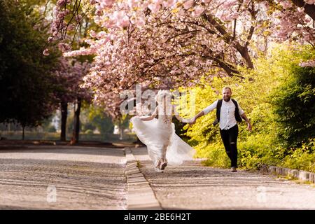 des jeunes mariés joyeux qui naissent dans la ville sont heureux parmi les arbres fleuris. Les jeunes mariés ont du plaisir à passer leur temps dans une belle ville. Mariage en spr Banque D'Images