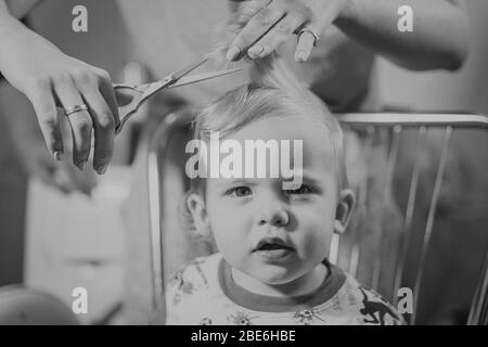 Première coupe de cheveux de petit garçon de bébé à la maison par les parents. Portrait noir et blanc. Effet de filtre à grain rétro Banque D'Images