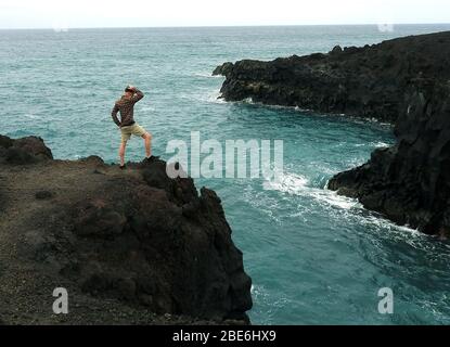 Un homme se tient sur le bord de la falaise à Los Hervideros, Timanfaya, Parc National volcanique, Lanzarote, îles Canaries, Espagne - Janvier 2020. Banque D'Images