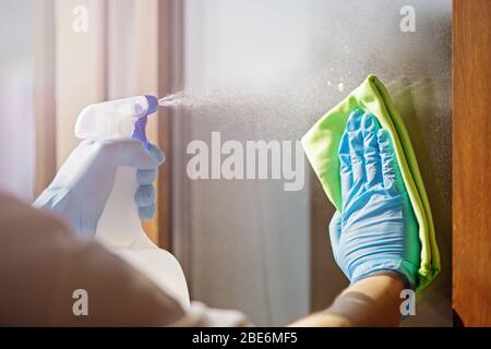 Fermez les mains dans la fenêtre de nettoyage des gants bleus avec du chiffon vert et du spray. Concept de travaux ménagers Banque D'Images