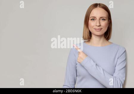 Gros plan portrait de jolie femme européenne avec des cheveux courts, indique avec index à l'espace vierge de copie, montre place pour votre annonce, isola Banque D'Images