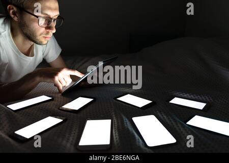 Dépendance, nomophobie, insomnie, troubles du sommeil. Gadget accro homme utilisant une tablette tard dans la nuit, chat sur les réseaux sociaux, allongé dans le lit autour de la Banque D'Images