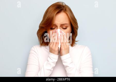 Portrait de la jeune femme effrayée dans un col de cygne blanc avec nez soufflant de serviette, yeux fermés, isolé sur fond bleu. Rhinite, poussière et assaisonnement à pollen Banque D'Images