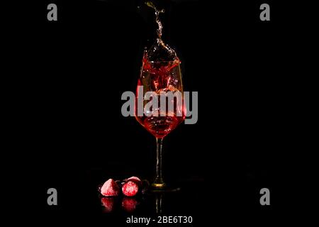 vin rouge ou rose éclaboussant d'un verre à vin sur fond noir avec des baies. Touche de vin Banque D'Images