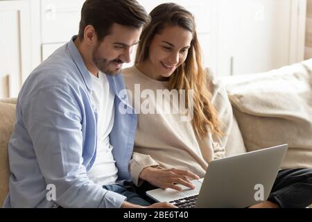Un couple de jeunes familles heureux assis sur le canapé, à l'aide d'un ordinateur. Banque D'Images
