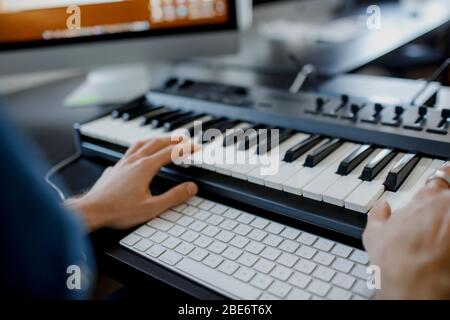 compositeur se charge des touches de piano dans le studio d'enregistrement. technologie de production musicale, l'homme travaille sur pianino et clavier d'ordinateur sur le bureau. gros plan Banque D'Images