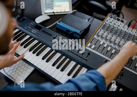 compositeur se charge des touches de piano dans le studio d'enregistrement. technologie de production musicale, l'homme travaille sur pianino et clavier d'ordinateur sur le bureau. gros plan Banque D'Images