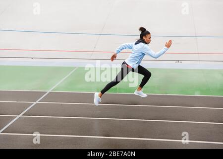 Belle jeune femme de sport africaine portant des écouteurs sans fil en cours de course au stade Banque D'Images