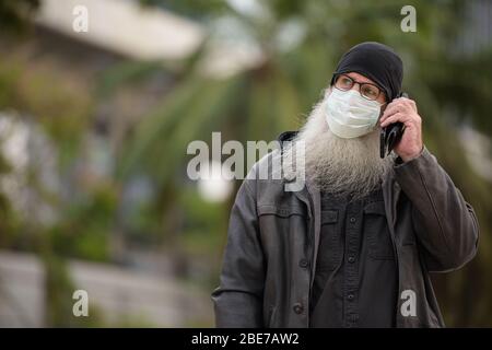 Homme taille babearded avec masque parlant sur le téléphone à l'extérieur Banque D'Images