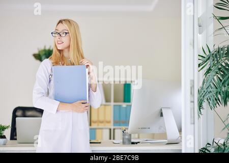 Jolie jeune femme souriante médecin dans un dossier de travail avec histoire médicale et regardant loin Banque D'Images