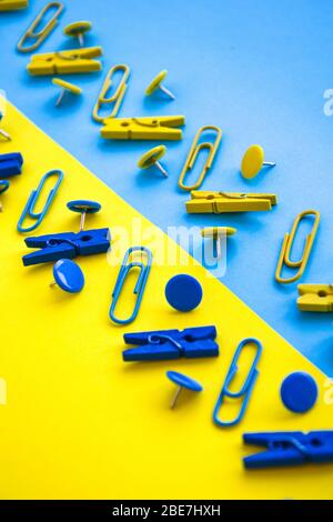 Fournitures de bureau sous forme de boutons et de trombones de couleur, de clous de giroches sur fond jaune et bleu, espace de copie Banque D'Images