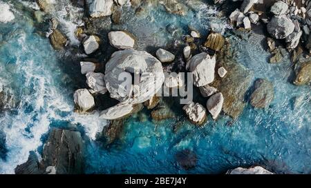 Une prise aérienne au-dessus d'un homme s'est abattée sur la roche dans la rivière bleue en Nouvelle-Zélande. Banque D'Images