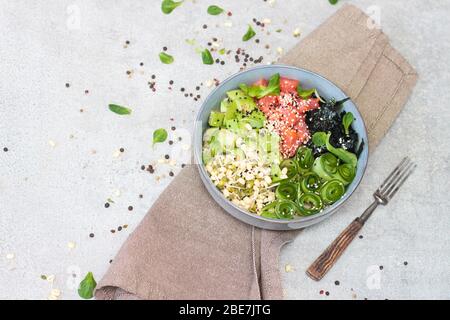 Bol à picoter avec saumon fumé, concombre, avocat, chou de mer, pousses de haricots, jeunes épinards, sésame et herbes. Arrière-plan gris, espace de copie. Banque D'Images