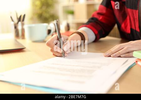 Gros plan sur les mains de la jeune fille étudiante signer le contrat sur un bureau à la maison Banque D'Images