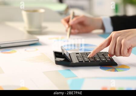 Gros plan de la femme de direction calcul avec calculatrice comparant les graphiques assis sur un bureau dans le bureau Banque D'Images