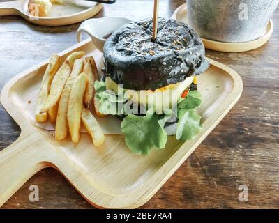 Hamburger au charbon de bois composé de pain au charbon noir et de sésame servi avec des frites de pommes de terre sur bois. Banque D'Images