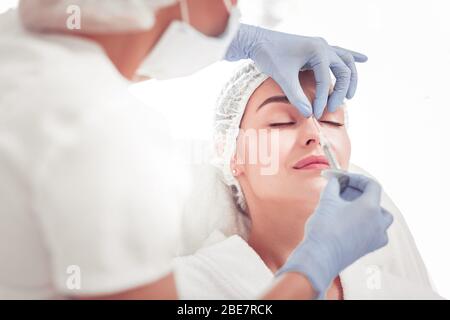 Photo de beauté. Coséologue qui pleurant des gants faisant de la beauté tourné dans la partie supérieure du nez Banque D'Images