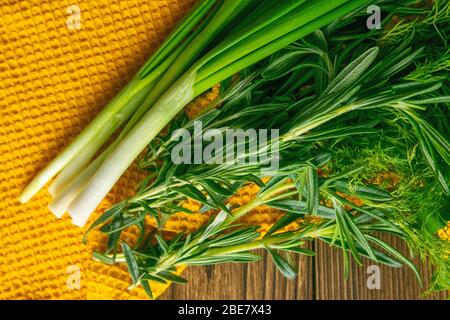 Légumes verts mélangés, frais, herbes de jardin. Épinards, romarin, aneth et oignons verts sur un support de serviette orange sur une table en bois. Vues de dessus, gros plan Banque D'Images