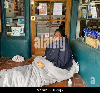 Santa Barbara, Californie, États-Unis. 12 avril 2020. La situation des sans-abri devient de plus en plus désasissante lorsque le virus Corona frappe la pleine force des rues. La deuxième victime de Covid-19 à mourir à Santa Barbara était un homme sans abri. Ici, une femme qui dort habituellement sur un banc de parc sur State Street, Santa BarbaraÃs principale artère, prend un abri sous un auvent devant le paradis trouvé, une librairie métaphysique fermée en raison du virus Corona, Et est heureux de recevoir un sandwich d'un volontaire de la Synagogue juive, Congrégation BÃnai BÃrith. Crédit: Amy Katz/ZUMA Wire/Alay Live News Banque D'Images