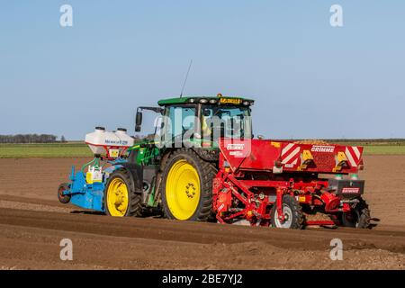 2018 accessoire John Deere Tracotr & Grimme Malpas vert plantant des pommes de terre de semence à Tarleton. Après une nuit froide avec un léger gel, les sols sont en bon état pour le labourage et la formation des rainures profondes à sillons à des fins de drainage, pour permettre la plantation par ressort de récoltes agricoles à l'aide d'un accessoire Grimm Malpas et d'un engrais avant avec un tracteur John Deere 6135R. Les cultures principales ou les terres d’arais comprennent des pommes de terre de type «maris Piper» et prennent de 16 à 22 semaines pour mûrir. Les pommes de terre de semence sont prêtes à planter lorsque les pousses «chit» après qu'elles commencent à gercer Banque D'Images