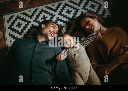 Jeune couple avec leur fils allongé sur le sol à la maison, pendant les loisirs dans le salon.