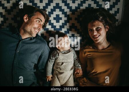Jeune couple avec leur fils allongé sur le sol à la maison, pendant les loisirs dans le salon.
