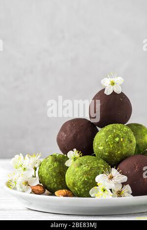 Boules d'énergie végétalienne brute faites de thé matcha, dattes et noix et boules dans le chocolat glacer avec fleurs de fleur de printemps. Style alimentaire. Un desseur végétalien sain Banque D'Images