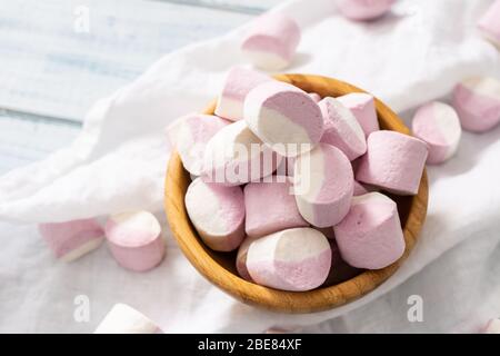 Bol en bois rempli de guimauves roses et blanches avec un peu dispersé autour d'un chiffon de table blanc. Banque D'Images