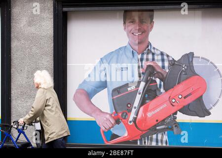 Une femme âgée qui utilise un cadre de marche passe devant un panneau pour une société de location d'outils tout en marchant sur Picton Road dans Urban Liverpool Banque D'Images