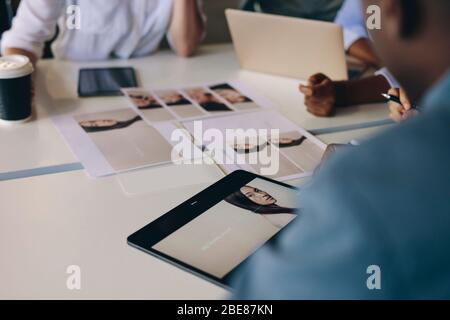 Groupe de professionnels qui choisissent du matériel pour un projet assis autour d'une table avec photo sur tablette numérique et photo-tirages. Banque D'Images